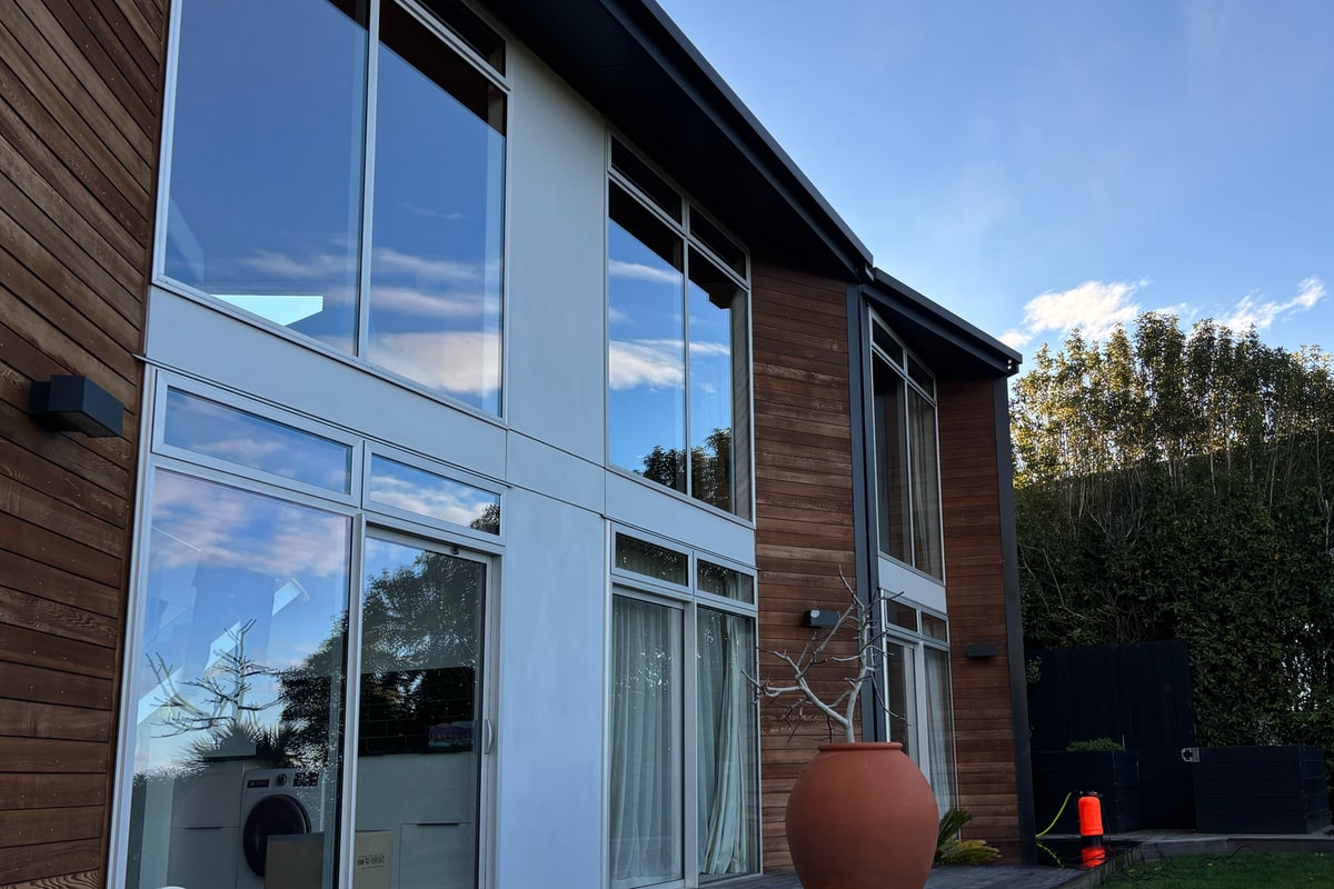 A cedar-clad Christchurch home with its windows clean, reflecting the evening sky