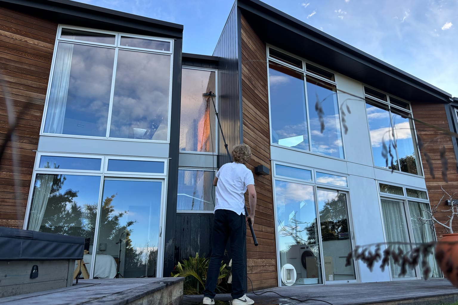 Luca cleaning the glass of a cedar-clad Christchurch house with a water-fed pole