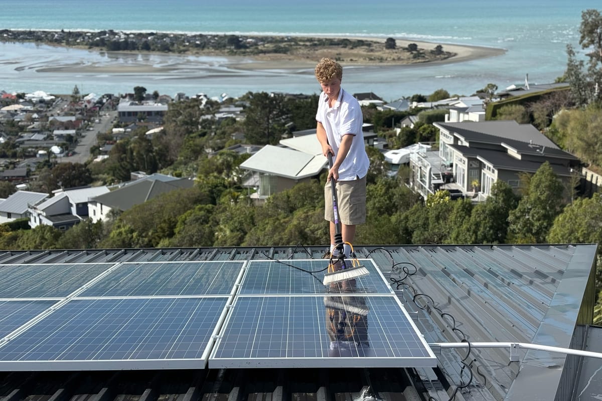 Luca cleaning roof-mounted solar panels with a pole, above the Christchurch estuary